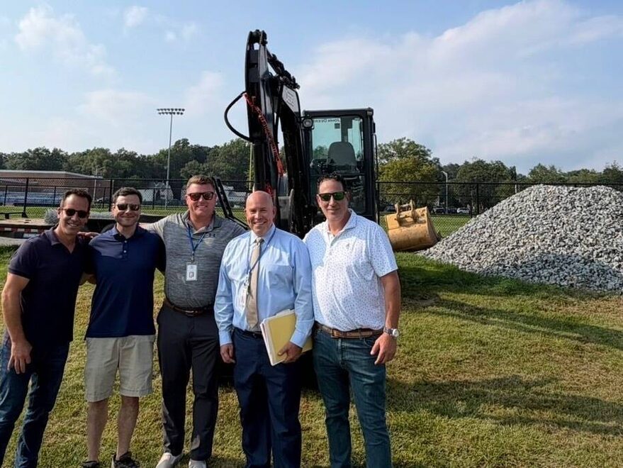 Five people standing in front of an excavator on a construction site