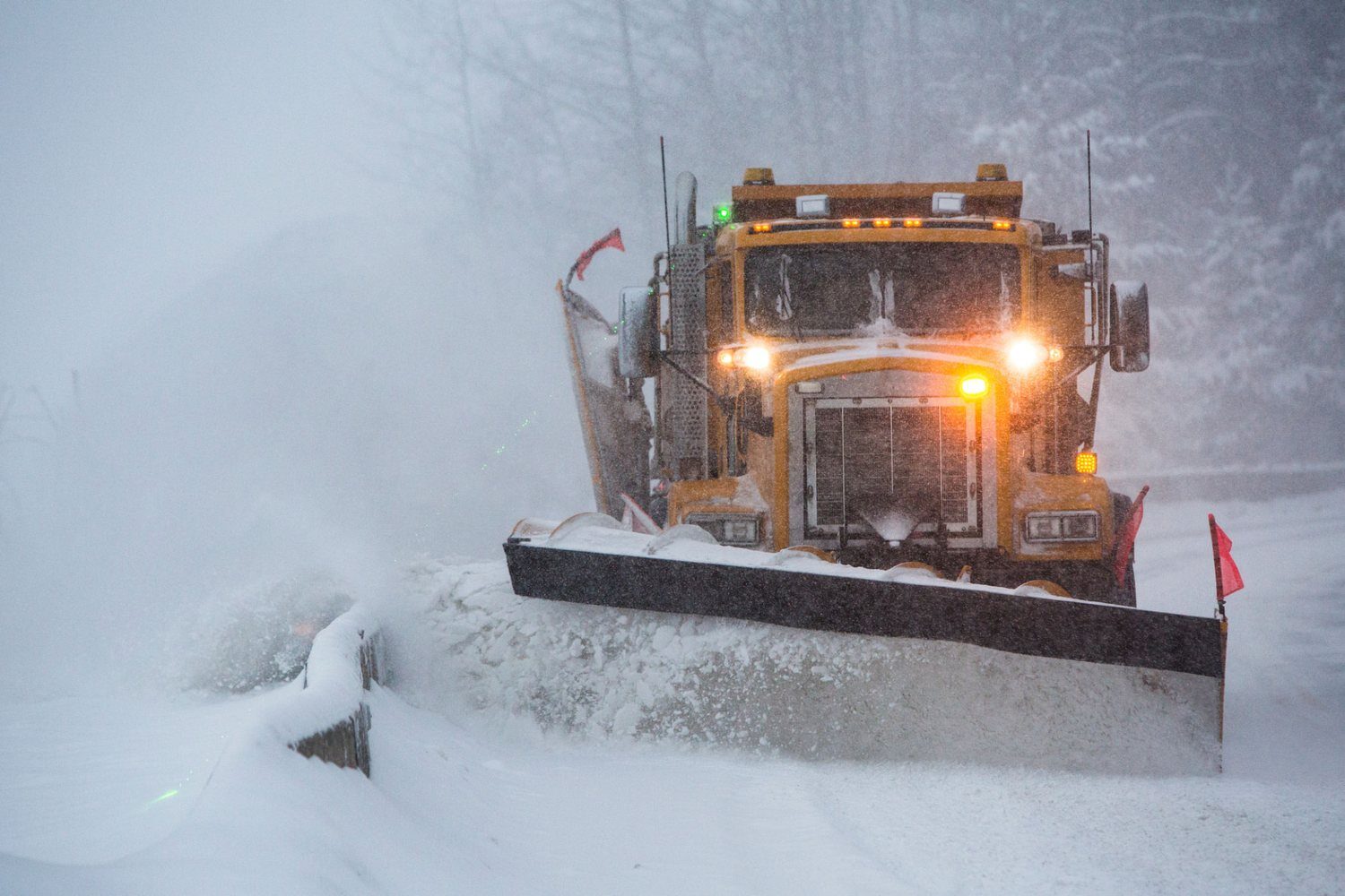 Snow plow clearing a road in a blizzard