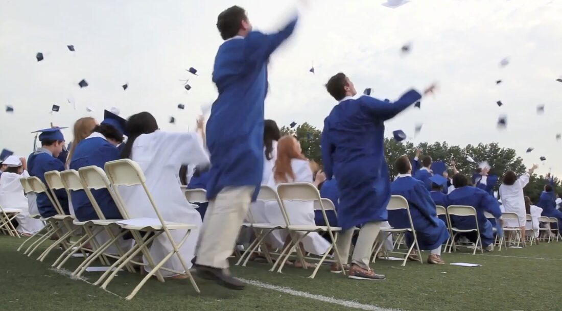 Graduates in blue gowns throwing their caps into the air at commencement